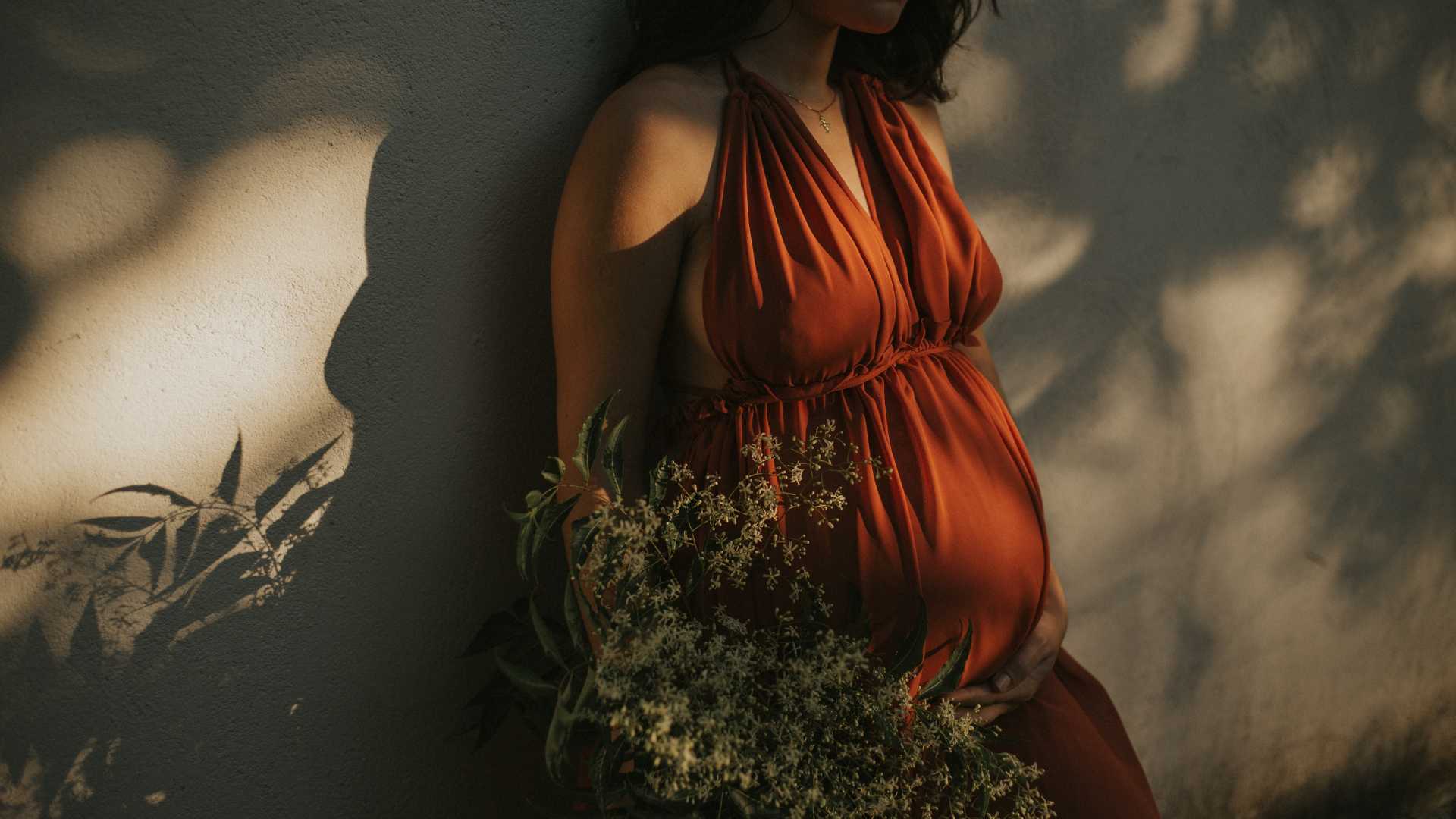 femme enceinte en robe orange avec un bouquet de fleur à la main
